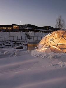 Snow piled up around a Growing Dome at dusk with a light inside