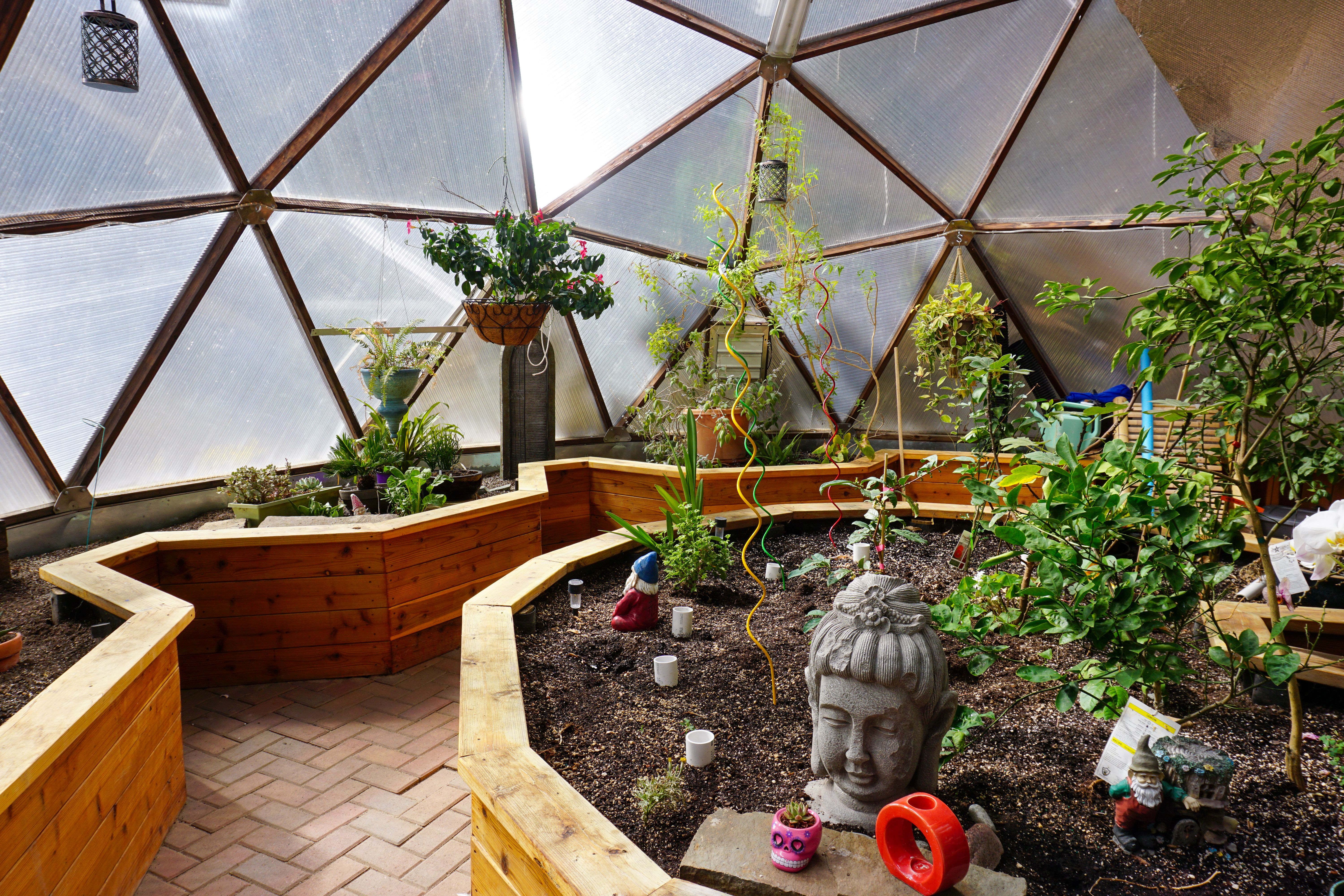 custom greenhouse interior design featuring a perimeter garden bed and a large central garden bed with various plants and statues