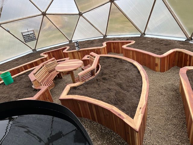 Custom greenhouse interior featuring redwood raised garden beds with built in bench and table