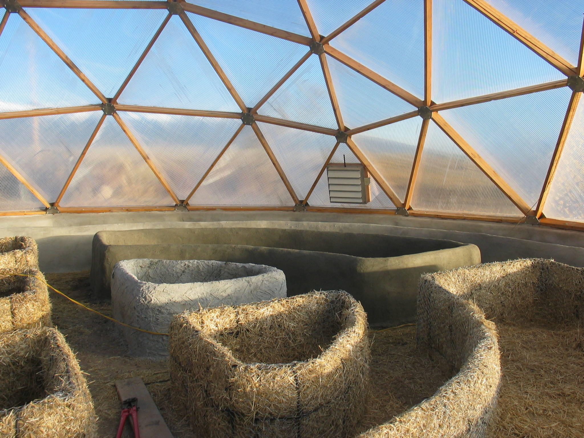 raised garden beds made of straw with plaster or stucco finish inside of geodesic dome greenhouse