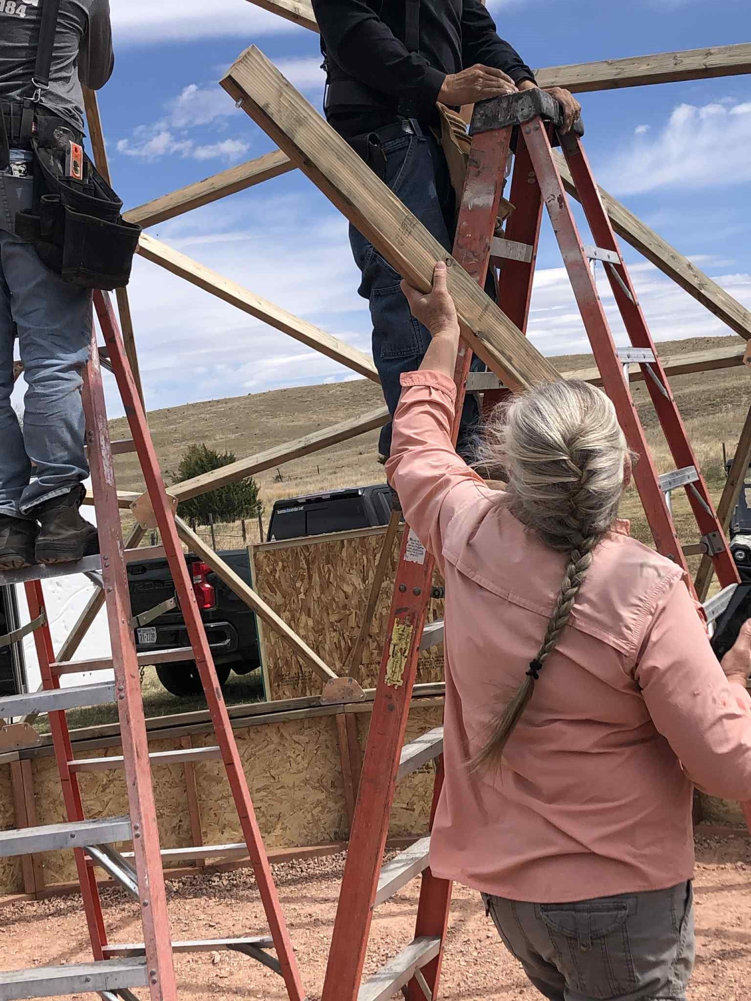 woman handing someone on a ladder a strut during dome construction