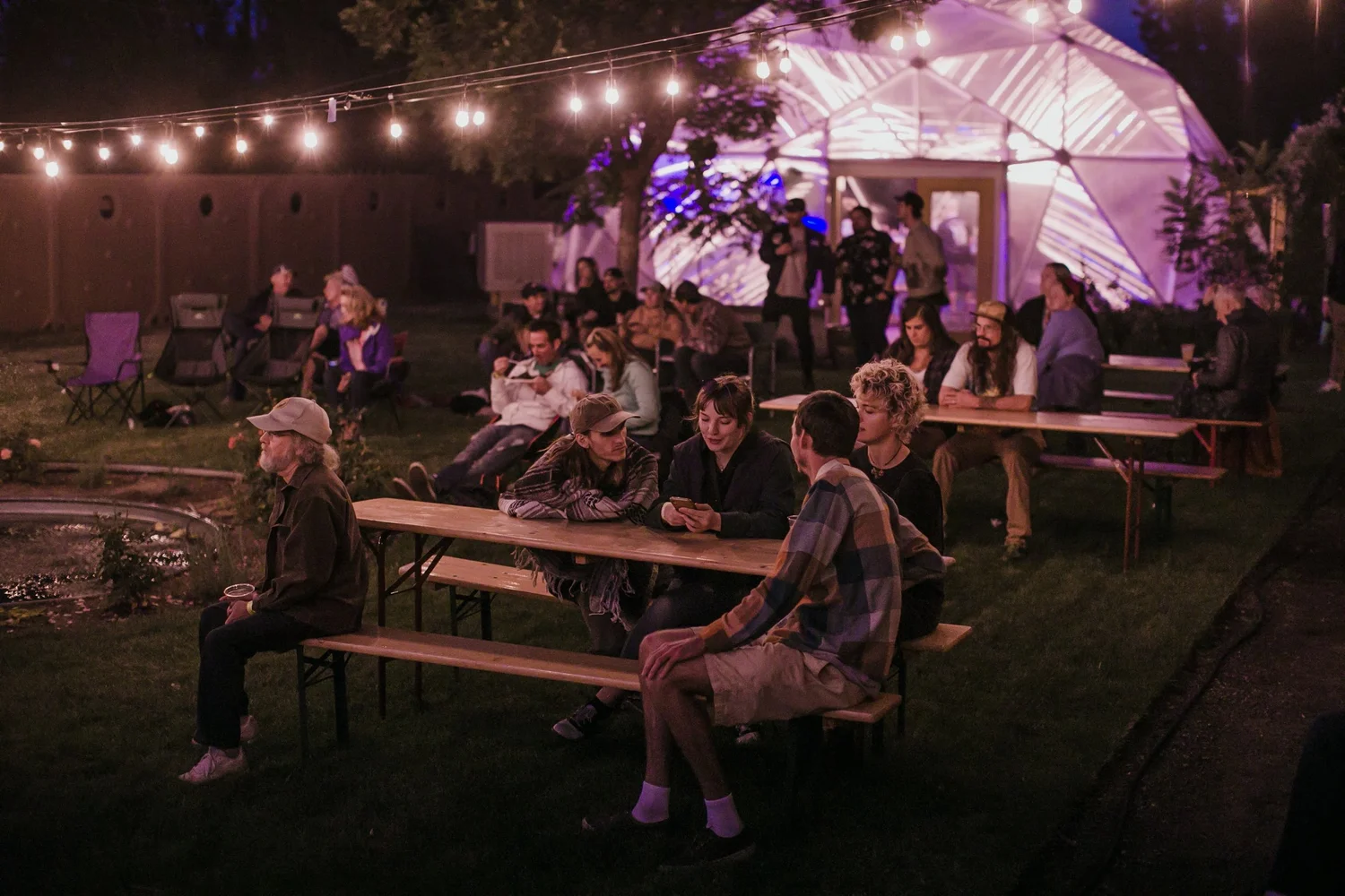 Community members gathered at tables outside a growing dome greenhouse at night
