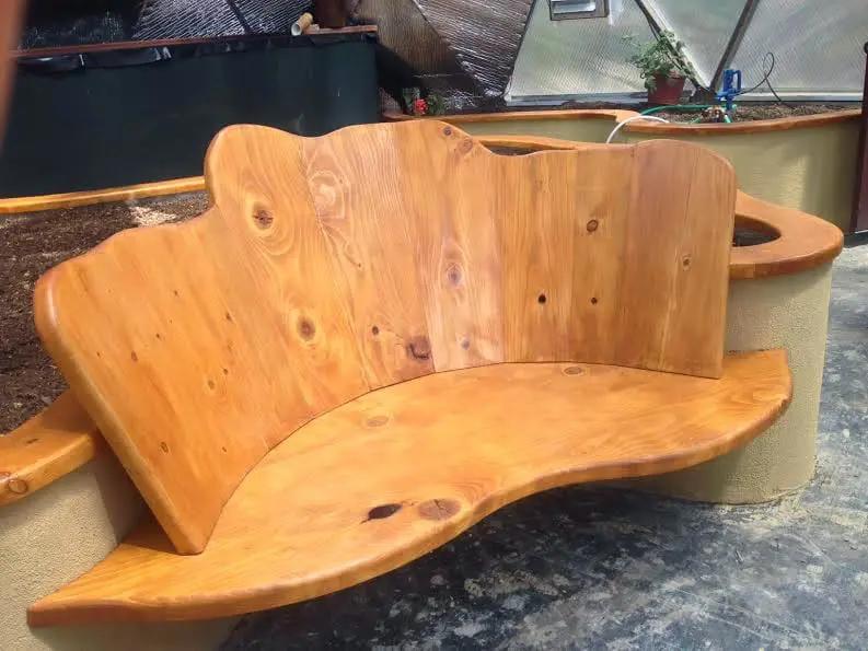 handmade wooden bench mounted on the outside of a raised garden bed inside the greenhouse