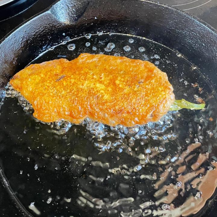 a golden fried stuffed chile in a cast iron skillet