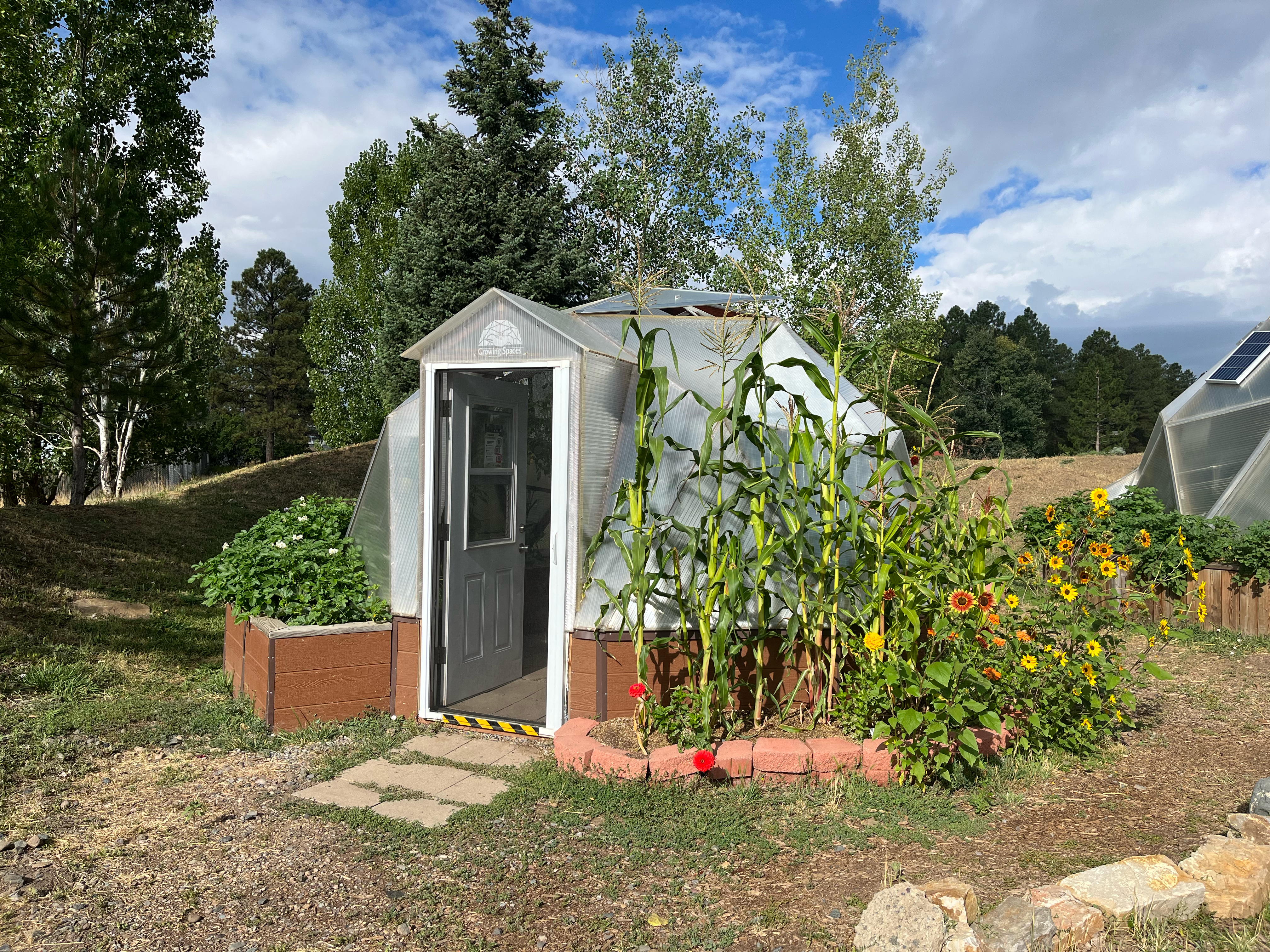 Growing Dome greenhouse in summer with open vents, door, and a fan.