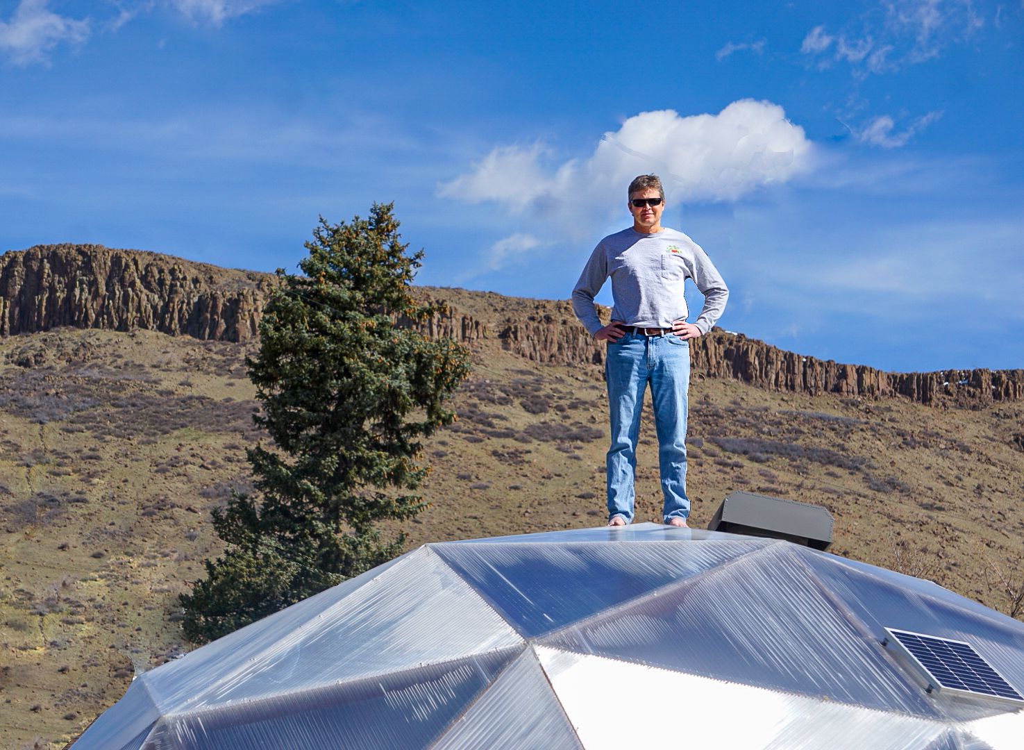 Man standing on top of a geodesic dome greenhouse