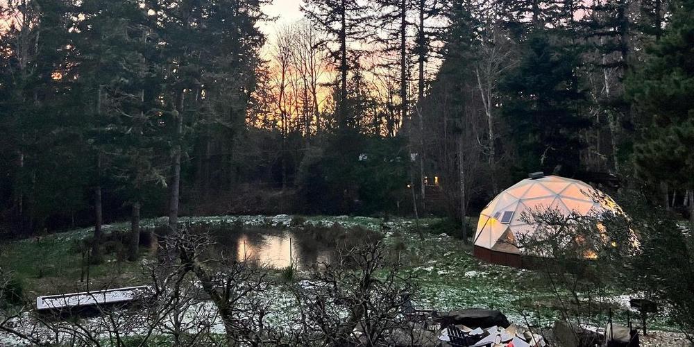 Growing Dome greenhouse in a forest setting with a light dusting of snow on the ground