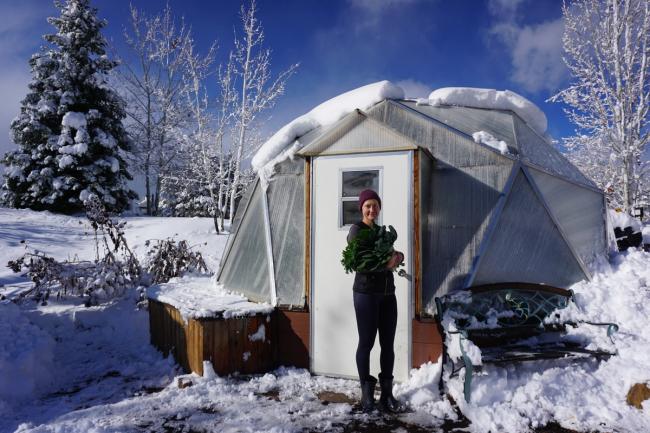 Gardener holding freshly harvested greens outside a snow-covered Growing Dome greenhouse