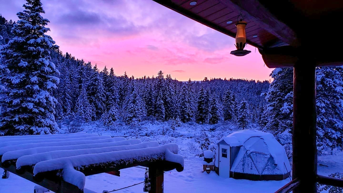 15 foot diameter geodesic greenhouse in Montana covered in snow with beautiful sunset colors in the sky.