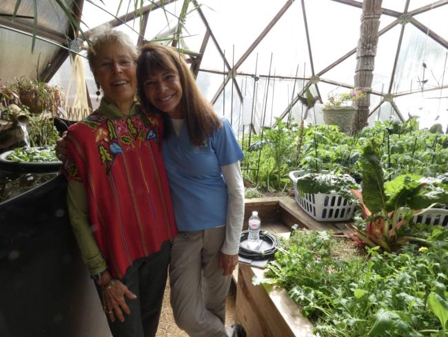 Two women posing for a photo in a Growing Dome greenhouse