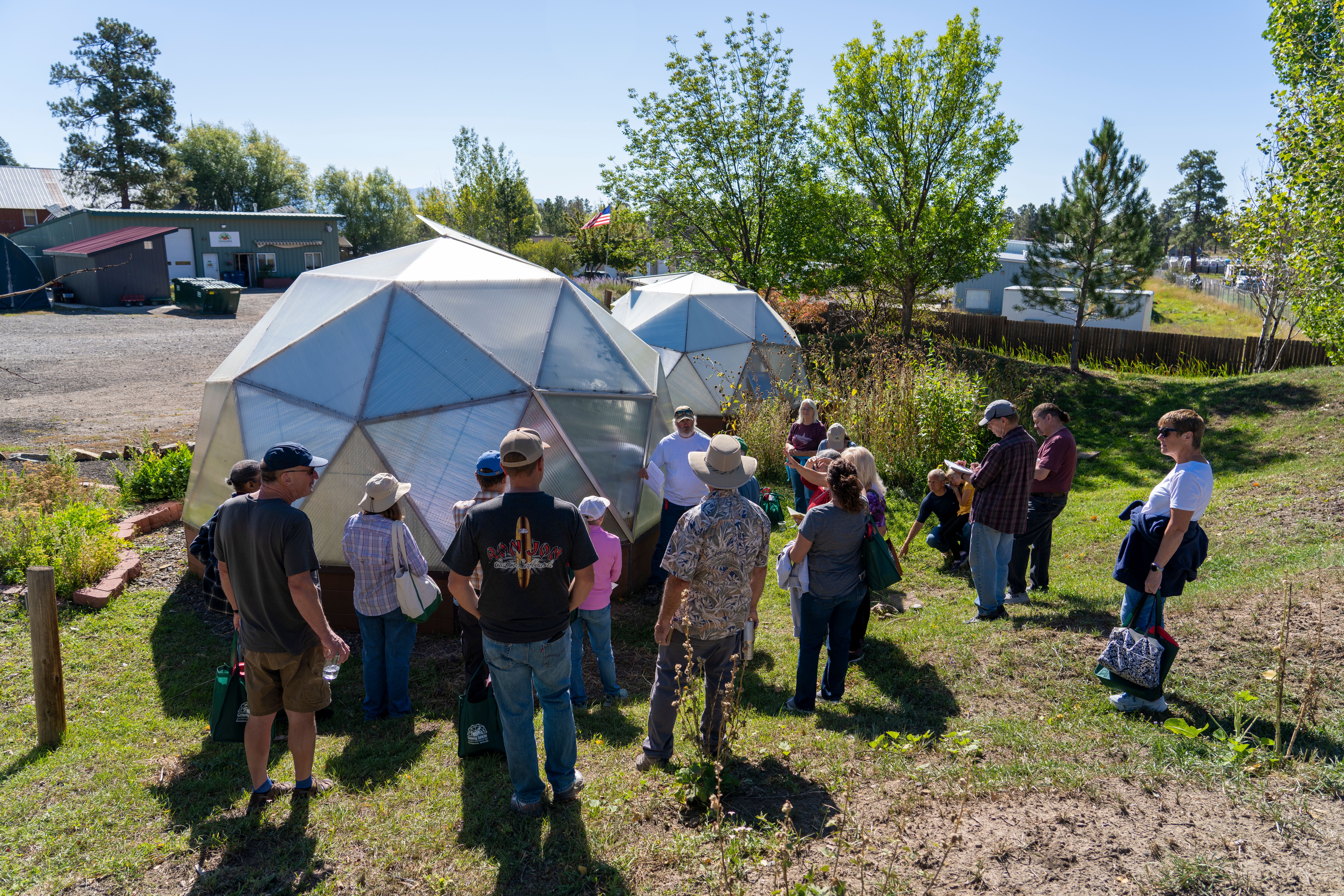 Group gathered around the outside of a Growing Dome greenhouse learning about maintenance procedures