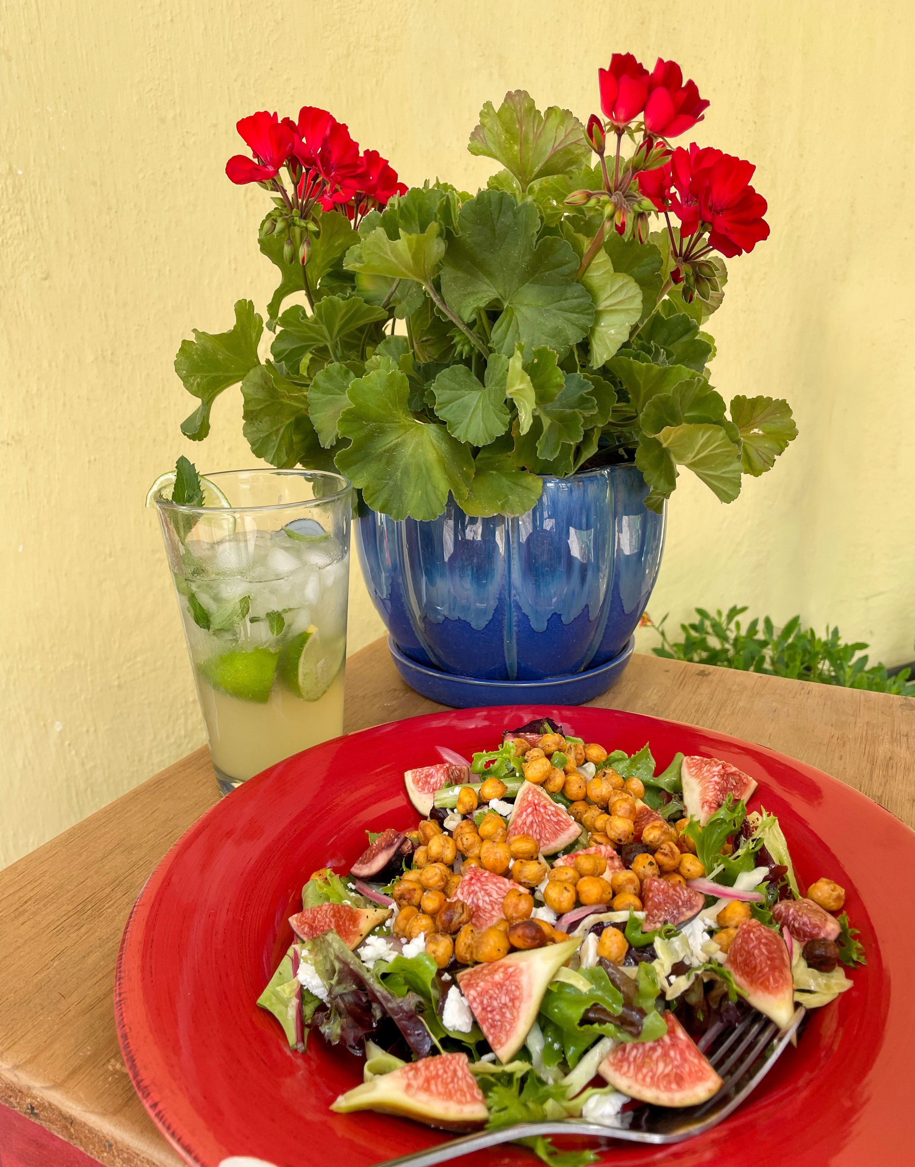 plated chickpea fig salad with mojito mocktail red geranium on table against yellow wall