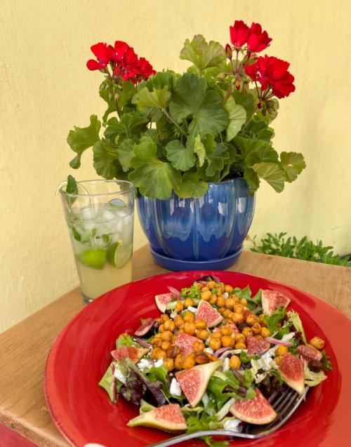 plated chickpea fig salad with mojito mocktail red geranium on table against yellow wall