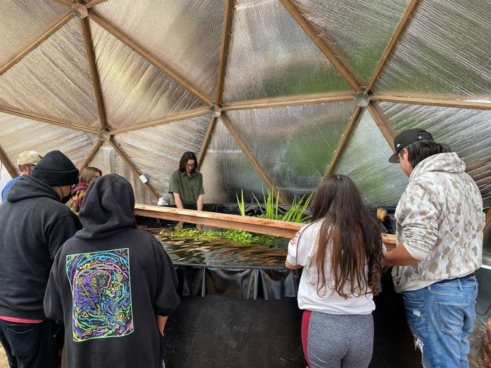 People standing around an above ground pond in a geodesic dome
