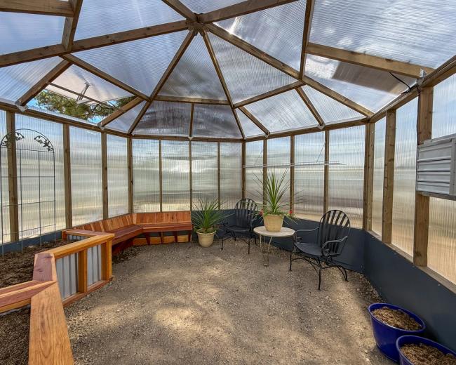 Interior of a Growzebo backyard greenhouse with redwood garden beds, benches and gravel floor