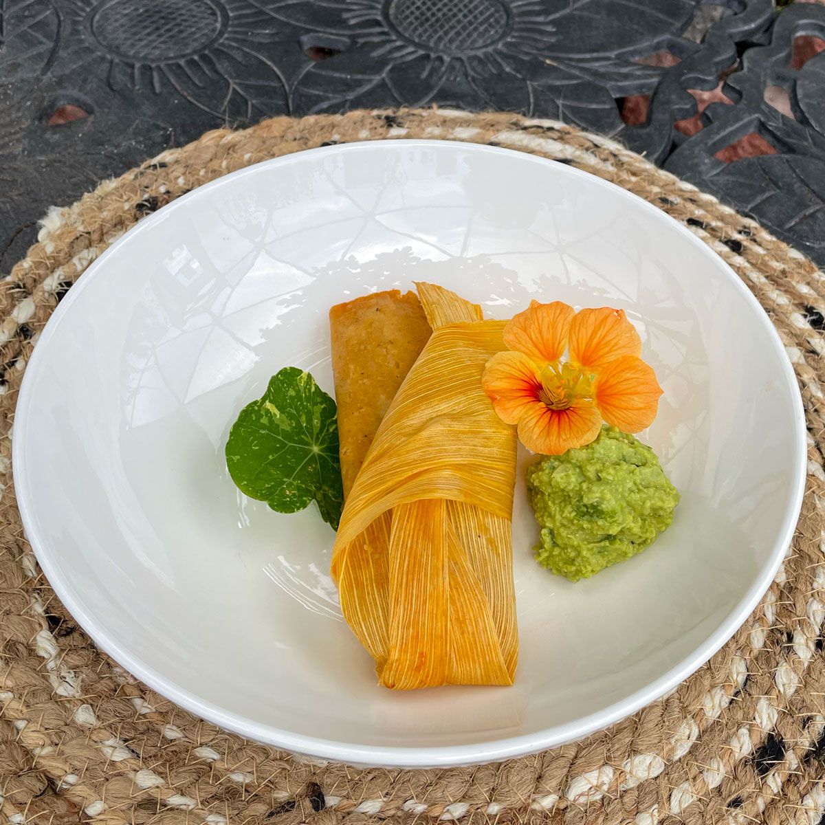 tamale plated with guacamole and garnished with nasturtium flower