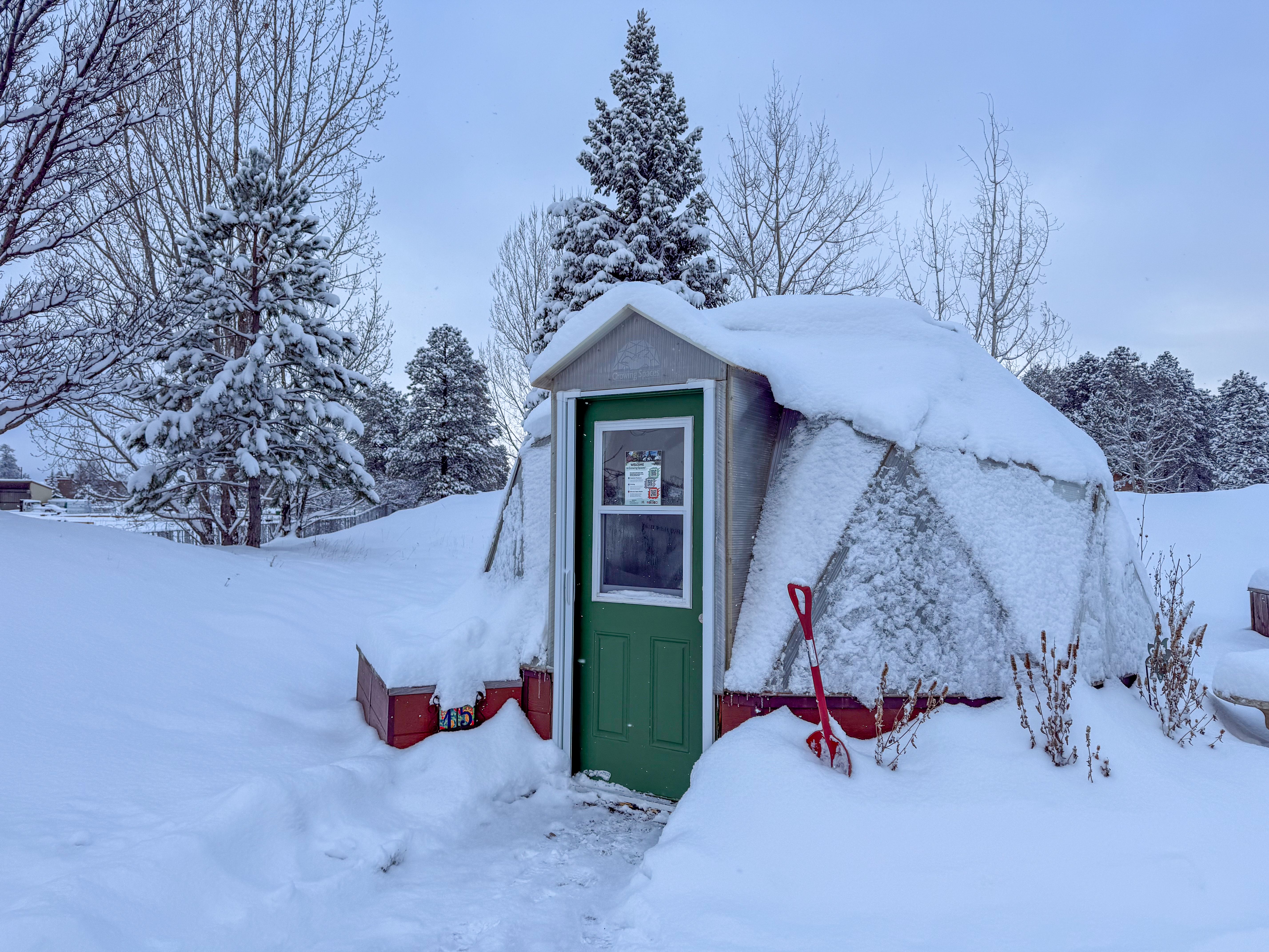 15 foot diameter growing dome with a green door covered in a blanket of snow