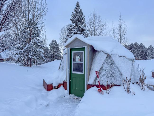15 foot diameter growing dome with a green door covered in a blanket of snow
