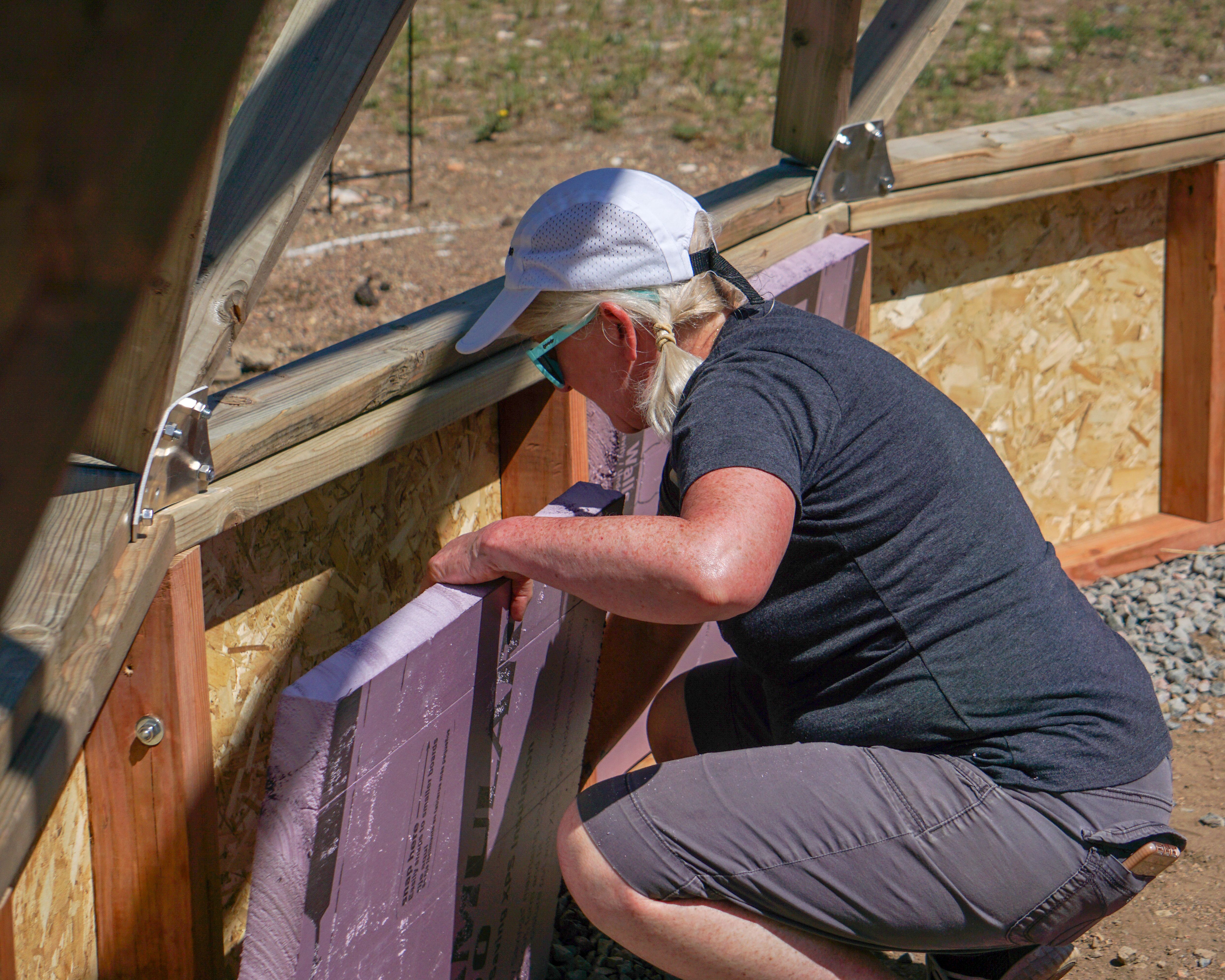 woman installing rigid foam insulation into the greenhouse foundation wall