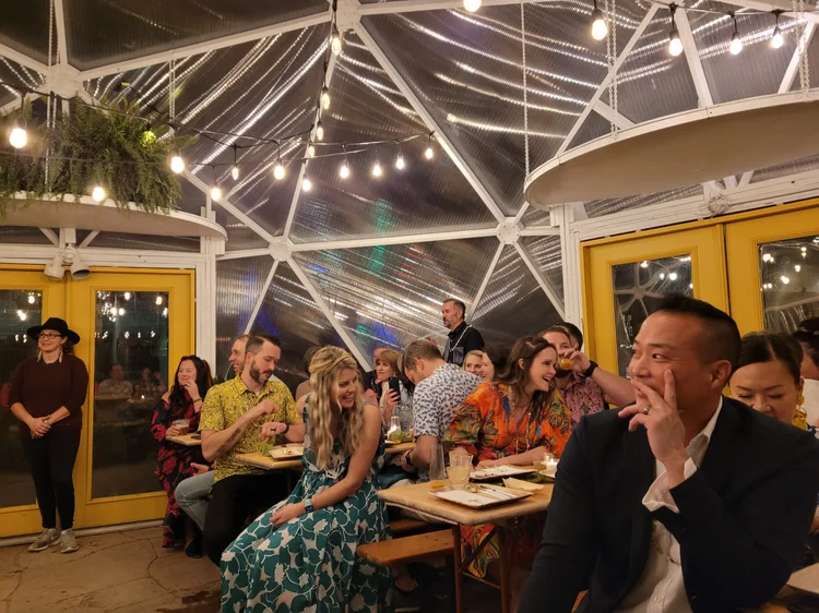 Large group of happy people inside a growing dome greenhouse with lights at night