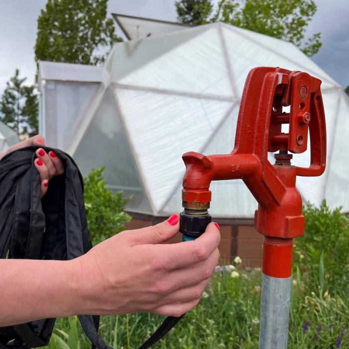 Watering best practices includes locating a spigot in close proximity to greenhouse, someone is attaching a hose