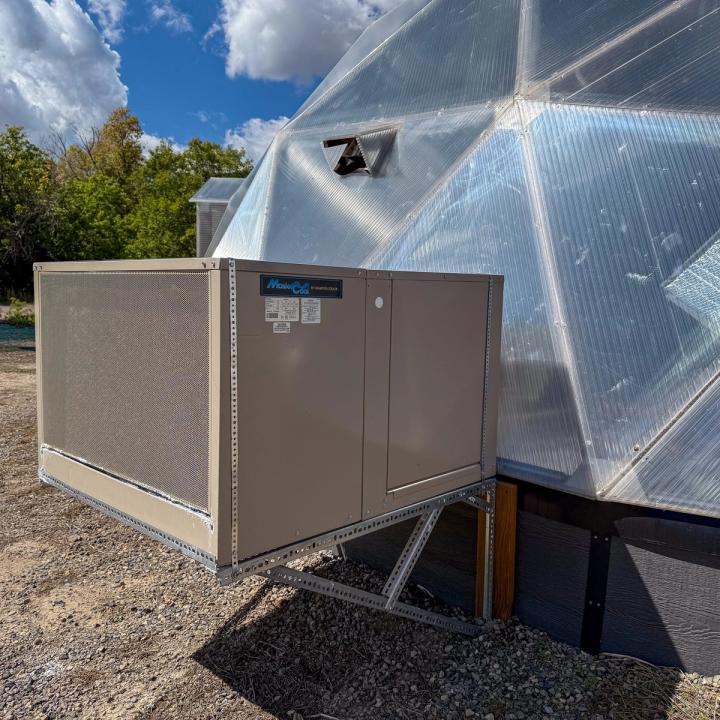 Evaporative cooler outside a Growing Dome geodesic greenhouse with a pollinator window mounted close by.