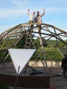 Customers proudly posing on ladders during the construction of their Growing Dome greenhouse