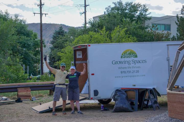 Growing Spaces supervisor holding up a piece sign and dome owner flexing her bicep in front of a Growing spaces trailer