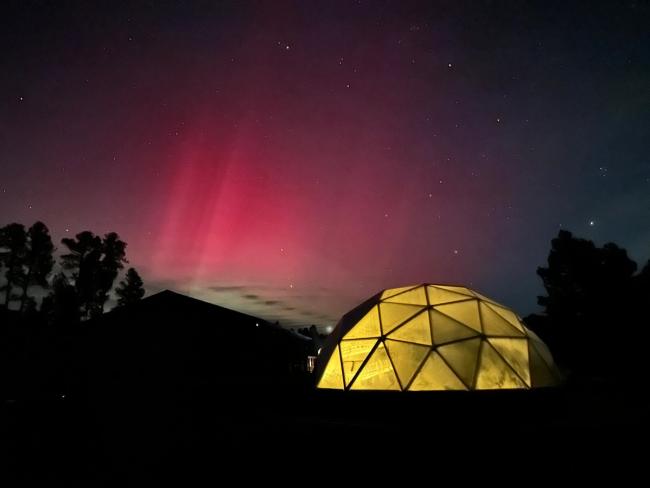 growing dome greenhouse lit up from inside at night with the aurora borealis in the sky