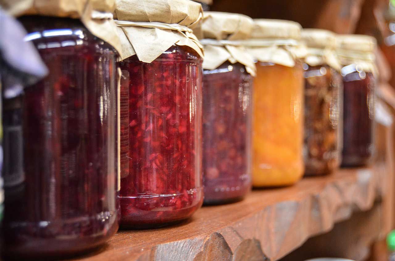 food preservation jars of jam lined up on a wooden shelf