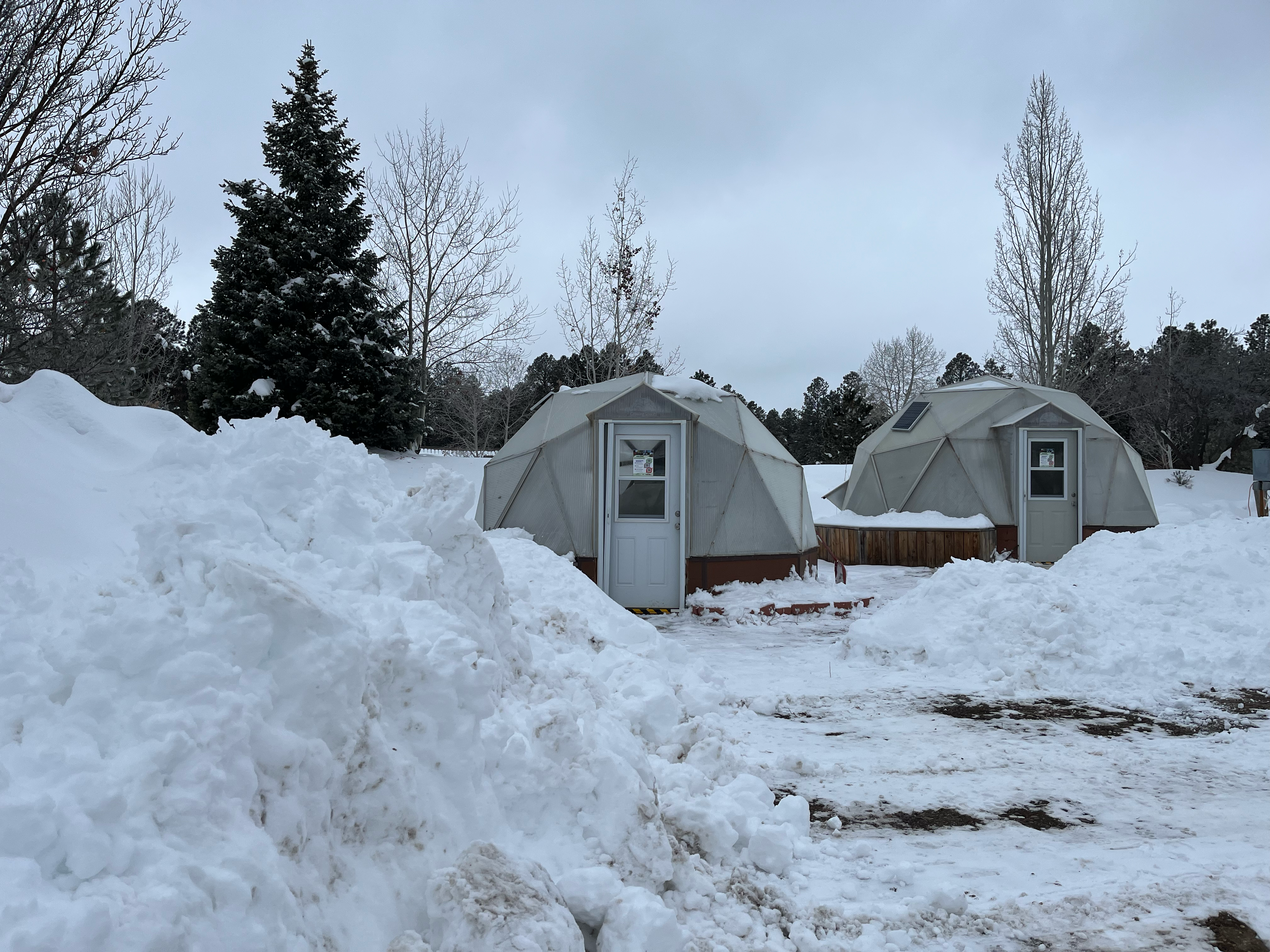 Two dome greenhouses surrounded by large piles of snow