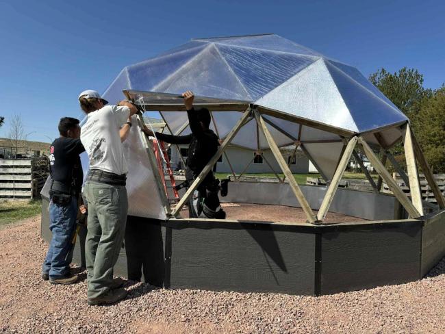 Workers installing polycarbonate panels and a vent on a 22' Growing Dome greenhouse