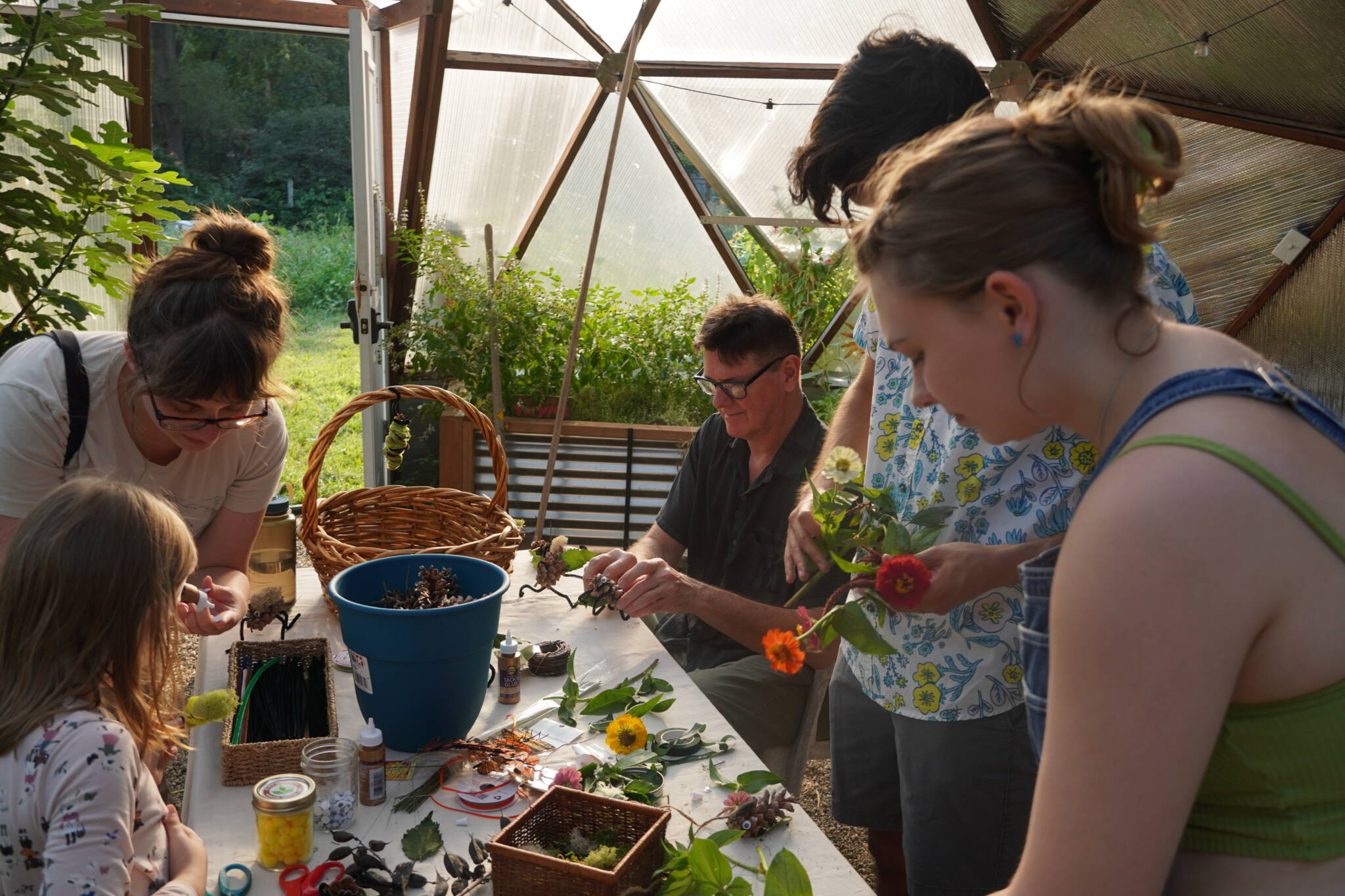 Community members seated around a table in a 26' Growing Dome creating flower bouquets