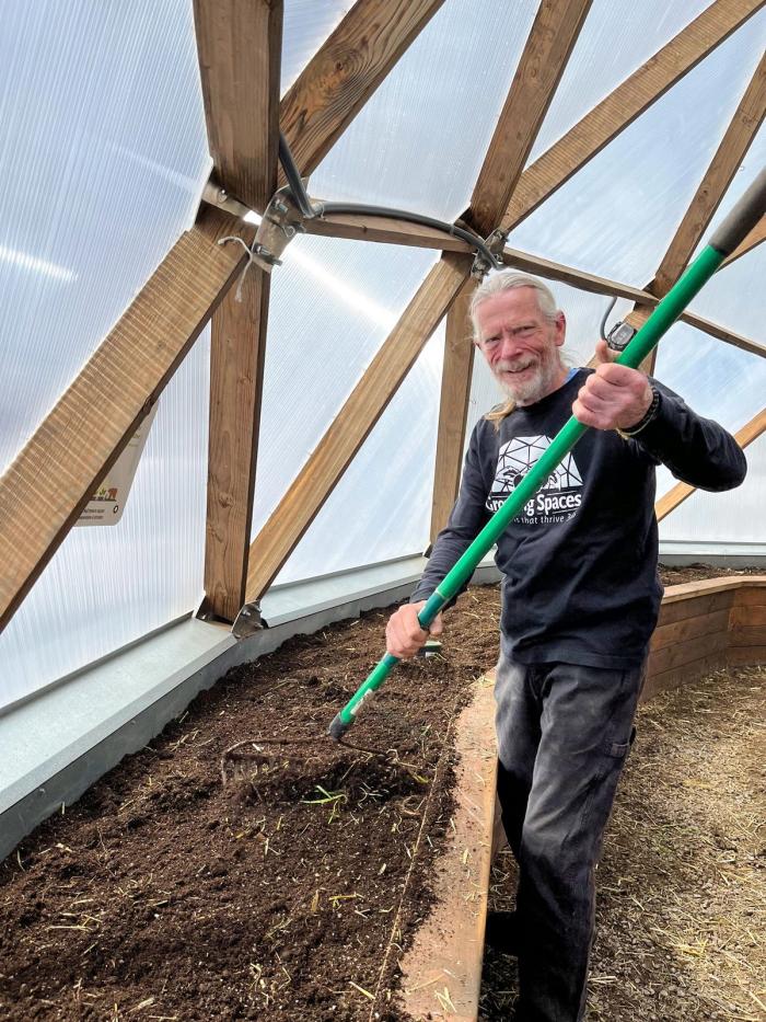 smiling growing spaces employee raking a raised bed inside a dome greenhouse