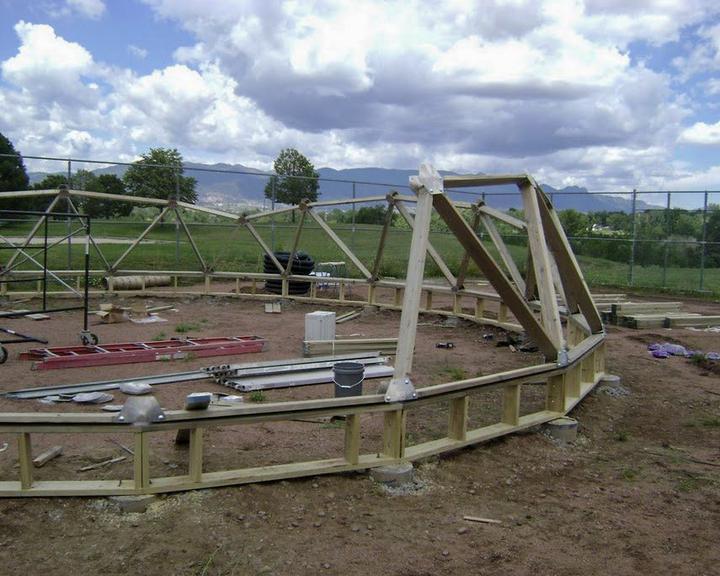 A partially assembled geodesic greenhouse on concrete piers