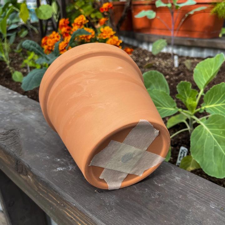 Terracotta pot with two pieces of masking tape placed on the underside of the pot to cover the drainage hole.