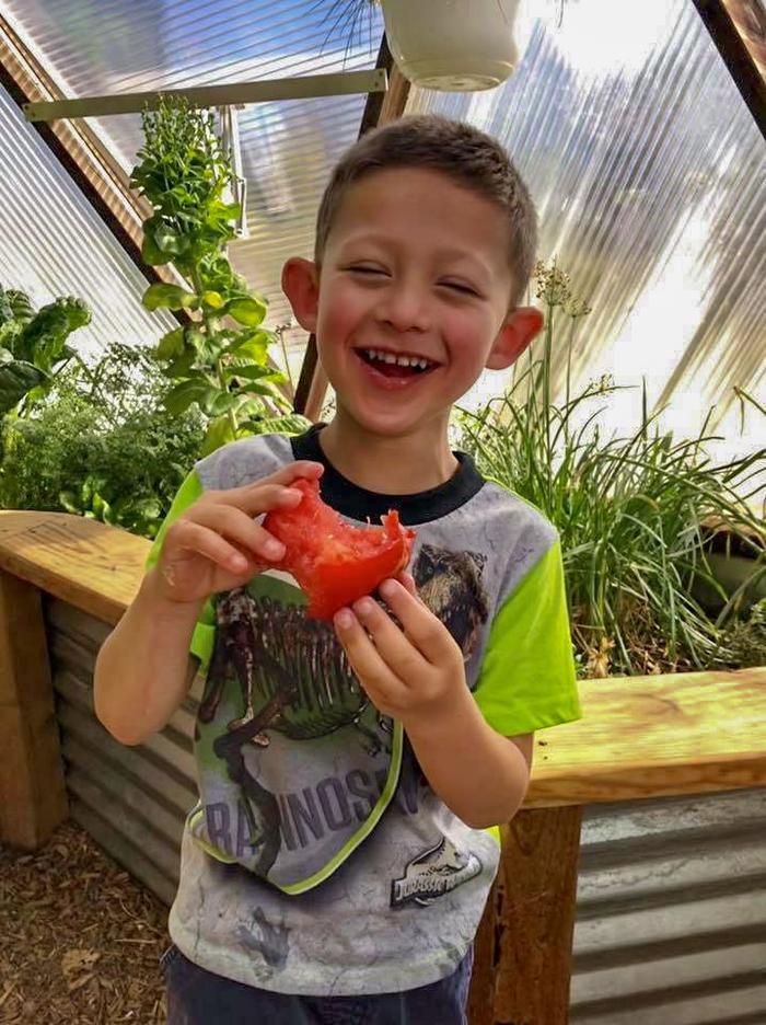 happy kid biting into a juicy tomato with a big smile on his face