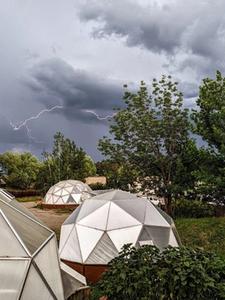 dark grey clouds with lightning bolts striking across the sky above three growing dome greenhouses