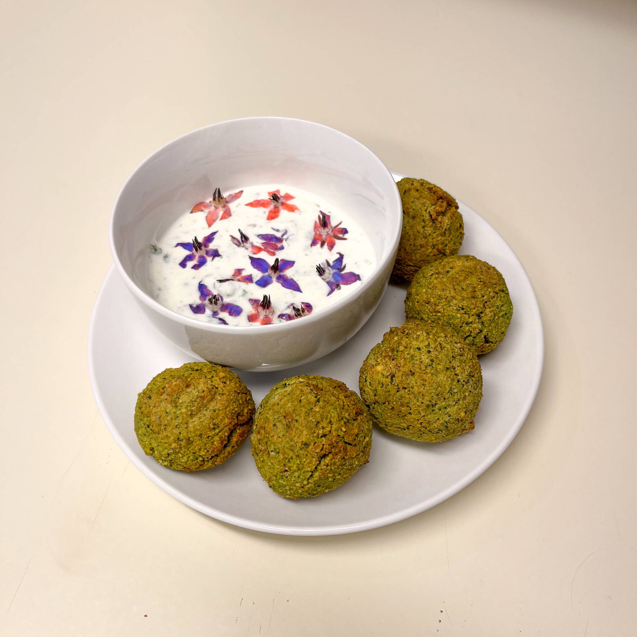 borage tzatziki sauce in a bowl garnished with flowers plated alongside falafel