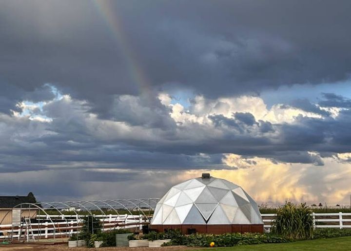 Growing Dome greenhouse with outdoor garden surrounding it and a hoop house frame to the left
