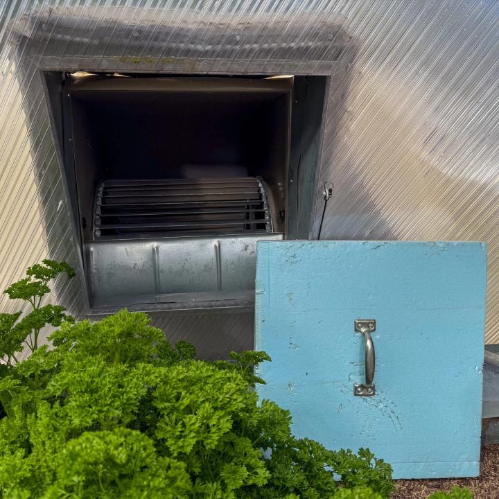 Evaporative cooler on the interior of a Growing Dome greenhouse with a blue board cover propped up next to it that is used in the winter.