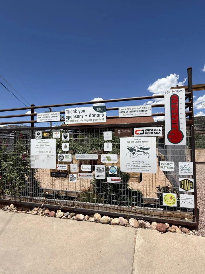Signs from various businesses and donors on a metal fence surrounding a community garden