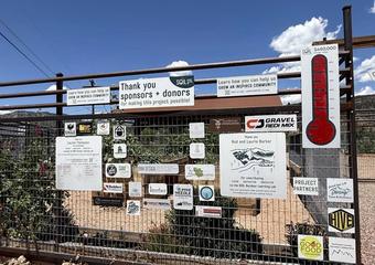 Signs from various businesses and donors on a metal fence surrounding a community garden