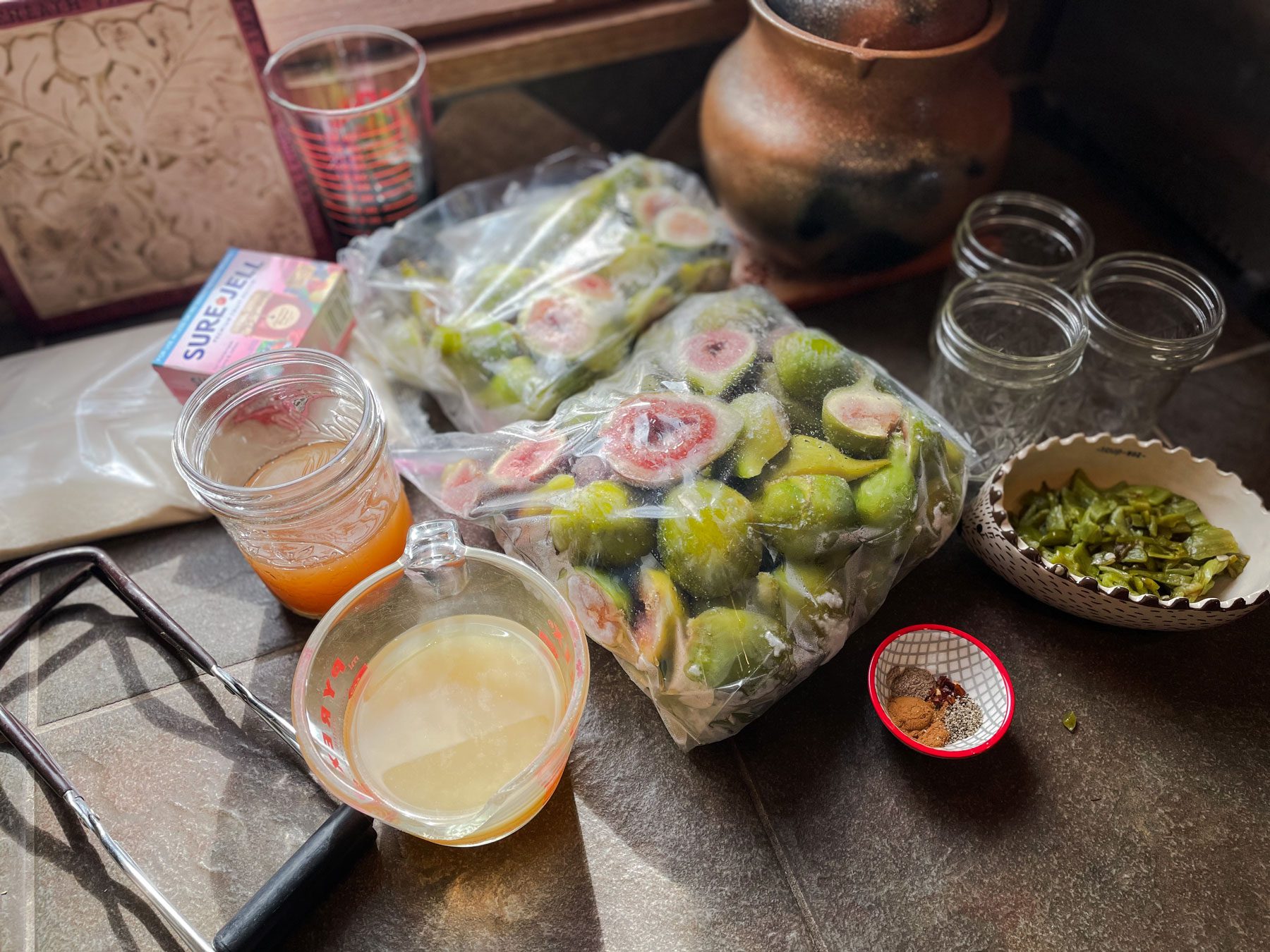 fig jam ingredients frozen figs chopped green chiles vinegar apple juice lime juice spices pectin jar lifter and glass jars sitting on a countertop