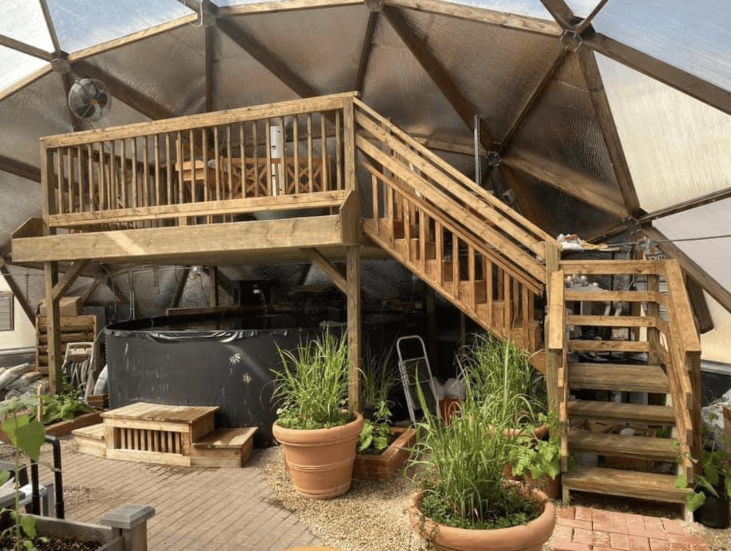 deck built over the above ground pond inside growing dome greenhouse