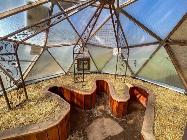 An asymmetric raised garden bed inside an 18' Growing Dome filled with straw and a large trellis