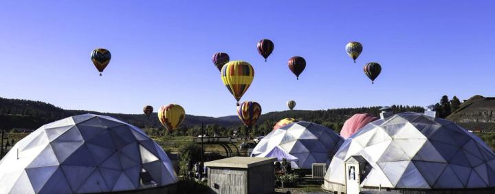 Three 42' Growing Domes in the foreground with thirteen brightly colored balloons ascending from the field behind them