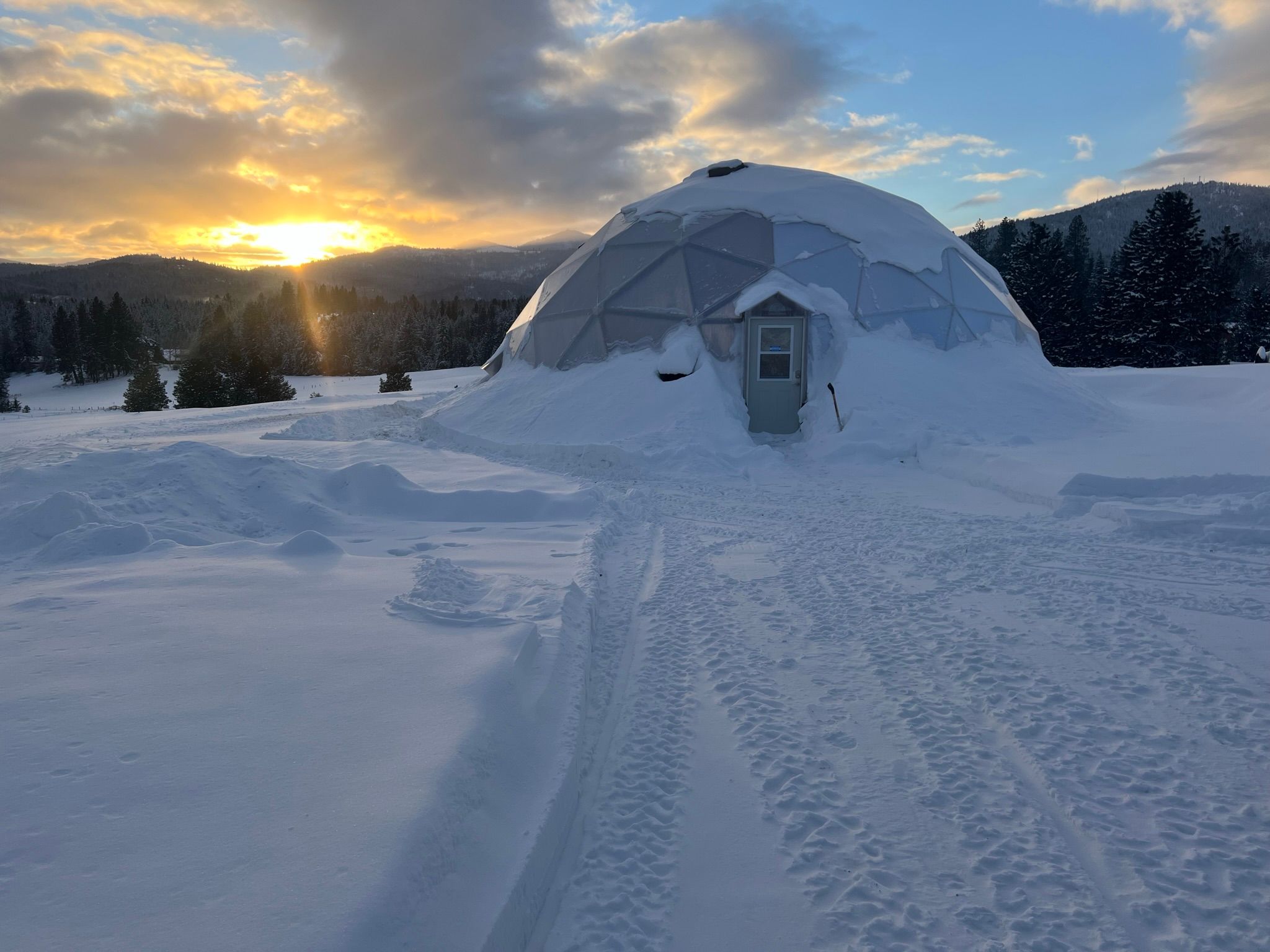 42 foot growing dome covered in snow with the sun setting behind a mountain