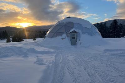 42 foot growing dome covered in snow with the sun setting behind a mountain
