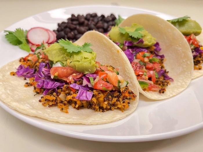 Three tacos filled with vegan taco meat made from quinoa, topped with red cabbage, salsa, and guacamole, on a plate with black beans.